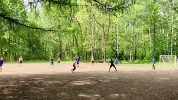 Rusia, San Petersburgo, 03 de junio de 2020: Los adolescentes juegan al fútbol en un campo de fútbol en el parque entre los árboles verdes, algunos chicos vestidos solo con pantalones cortos, claro tiempo soleado — Vídeos de Stock