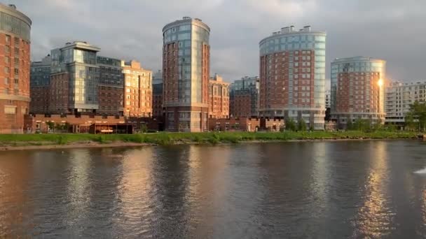 Rusland, Sint-Petersburg, 10 juni 2020: De boot met een wakesurfer op een golf stroomt bij zonsondergang de rivier af, een woonwijk op een achtergrond, zonnevlekken in ramen van gebouwen — Stockvideo