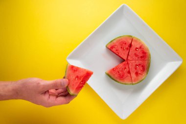 Sarı arka plana karşı bir tabakta dilimlenmiş karpuz toplama eli.