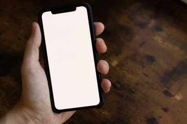Beyaz ekranlı bir telefonu tutan el. Ahşap arka plan ve copyspace.