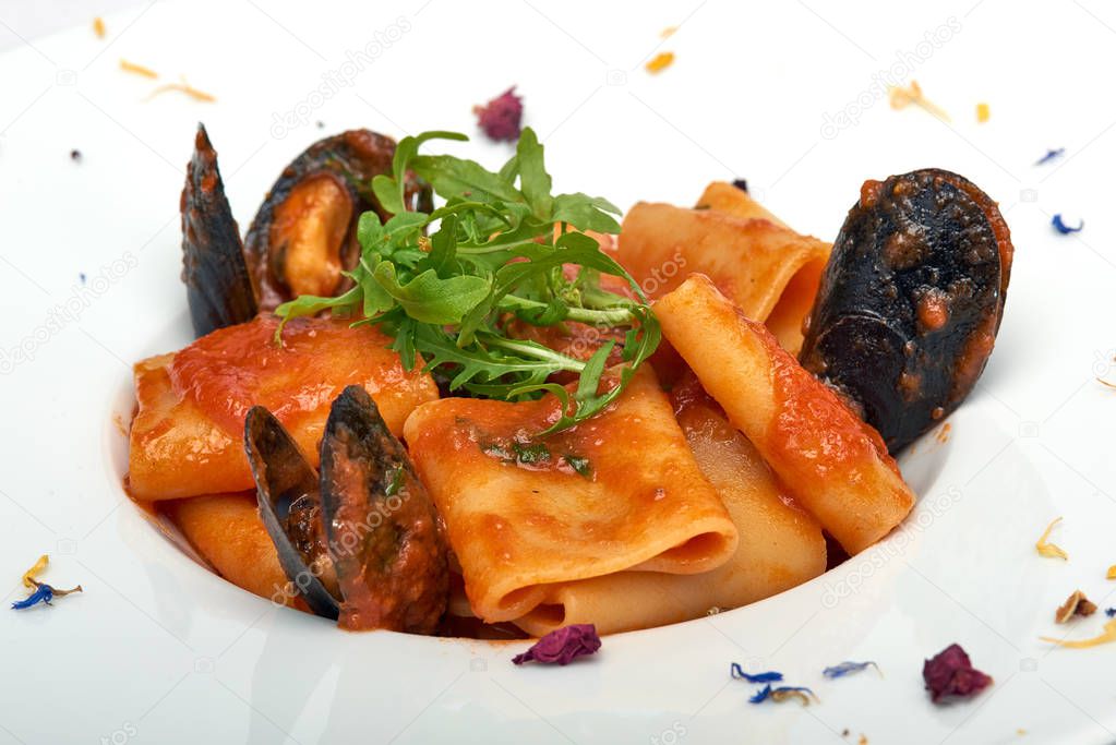 Italian food, Paccheri pasta with fresh mussels and rocket salad, served on white plate, isolated on white background