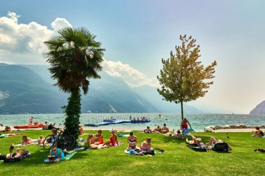 Bir Riva del Garda, Lago di Garda, İtalya - 21 Haziran 2018: banyo ve Lake Garda, güzel Garda Gölü yaz aylarında dağlarla çevrili, tan için sahilde oturup insanlar