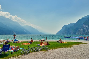 Bir Riva del Garda, Lago di Garda, İtalya - 21 Haziran 2018: banyo ve Lake Garda, güzel Garda Gölü yaz aylarında dağlarla çevrili, tan için sahilde oturup insanlar