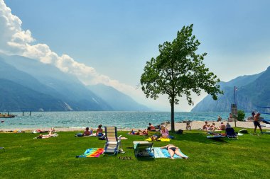 Bir Riva del Garda, Lago di Garda, İtalya - 21 Haziran 2018: banyo ve Lake Garda, güzel Garda Gölü yaz aylarında dağlarla çevrili, tan için sahilde oturup insanlar