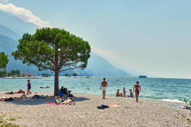 Bir Riva del Garda, Lago di Garda, İtalya - 21 Haziran 2018: banyo ve Lake Garda, güzel Garda Gölü yaz aylarında dağlarla çevrili, tan için sahilde oturup insanlar
