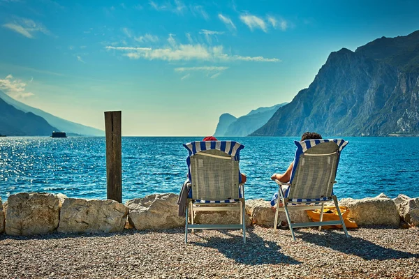 Plajda şezlong üzerinde oturan ve yaz saati, görünümü dağlarla çevrili güzel Lake Garda Garda Gölü hayran insanlar