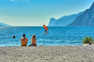 Torbole, İtalya-09 Ekim 2018: insanlar plajda şezlong üzerinde oturan ve yaz saati, görünümü dağlarla çevrili güzel Lake Garda Garda Gölü hayran