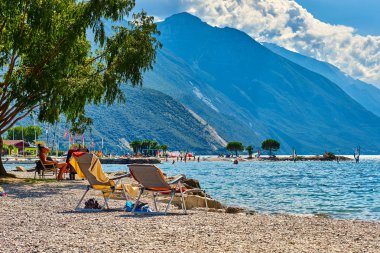 Torbole, İtalya-09 Ekim 2018: insanlar plajda şezlong üzerinde oturan ve yaz saati, görünümü dağlarla çevrili güzel Lake Garda Garda Gölü hayran