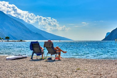 Torbole, İtalya-09 Ekim 2018: insanlar plajda şezlong üzerinde oturan ve yaz saati, görünümü dağlarla çevrili güzel Lake Garda Garda Gölü hayran