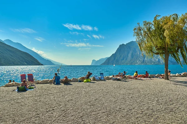 Torbole, İtalya-09 Ekim 2018: insanlar plajda şezlong üzerinde oturan ve yaz saati, görünümü dağlarla çevrili güzel Lake Garda Garda Gölü hayran