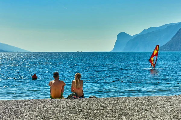 Torbole, İtalya-09 Ekim 2018: insanlar plajda şezlong üzerinde oturan ve yaz saati, görünümü dağlarla çevrili güzel Lake Garda Garda Gölü hayran