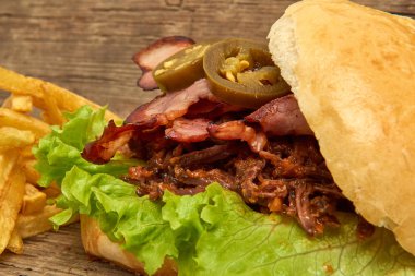 Barbekü çekti beff sandviç yeşil salata, gevrek domuz pastırması, acı biber jalapeno, Barbekü sos ve kişiler üzerine ahşap arka plan, Fast food