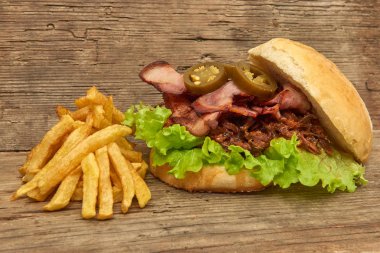 Barbekü çekti beff sandviç yeşil salata, gevrek domuz pastırması, acı biber jalapeno, Barbekü sos ve kişiler üzerine ahşap arka plan, Fast food