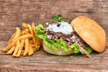 Barbekü çekti domuz sandviç Tzatziki sos, Barbekü sos ve patates ahşap zemin üzerine yeşil salata ile