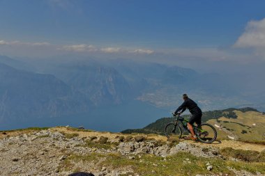 Monte Baldo, Lago di Garda, İtalya - 27 Mayıs 2016 dağ bisikleti adamı dağlar orman manzara yaz aylarında bisiklete binmek üzerinde. MTB dağ bisikletçinin Garda Gölü görünüme sahiptir