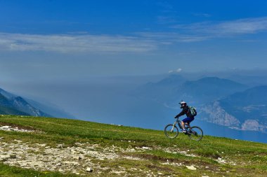 Monte Baldo, Lago di Garda, İtalya - 27 Mayıs 2016 dağ bisikleti adamı dağlar orman manzara yaz aylarında bisiklete binmek üzerinde. MTB dağ bisikletçinin Garda Gölü görünüme sahiptir