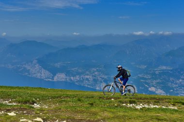 Monte Baldo, Lago di Garda, İtalya - 27 Mayıs 2016 dağ bisikleti adamı dağlar orman manzara yaz aylarında bisiklete binmek üzerinde. MTB dağ bisikletçinin Garda Gölü görünüme sahiptir