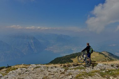 Monte Baldo, Lago di Garda, İtalya - 27 Mayıs 2016 dağ bisikleti adamı dağlar orman manzara yaz aylarında bisiklete binmek üzerinde. MTB dağ bisikletçinin Garda Gölü görünüme sahiptir