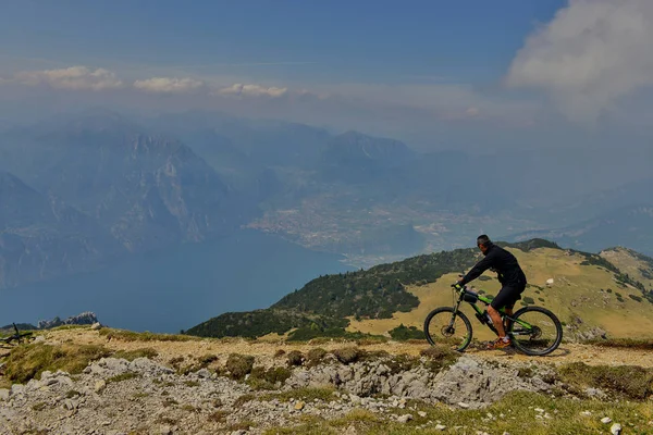 Monte Baldo, Lago di Garda, İtalya - 27 Mayıs 2016 dağ bisikleti adamı dağlar orman manzara yaz aylarında bisiklete binmek üzerinde. MTB dağ bisikletçinin Garda Gölü görünüme sahiptir