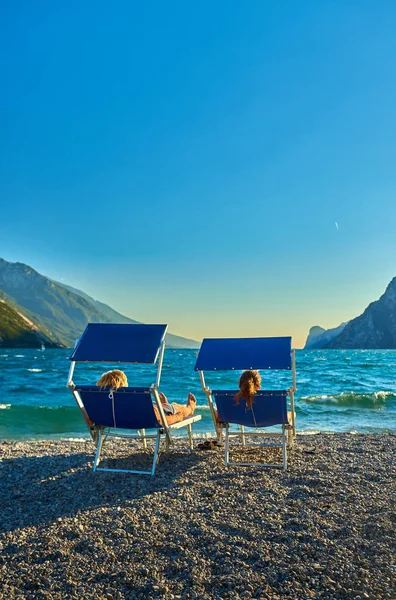 ビーチ ラウンジの椅子の上に座って 夏の時間 山に囲まれた美しいガルダ湖のビューでガルダ湖を眺めながらの — ストック写真