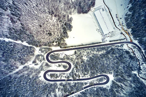 The aerial view of winding road from high mountain pass with snow-covered trees in Transylvania, Romania, Curved road view by drone in the winter time