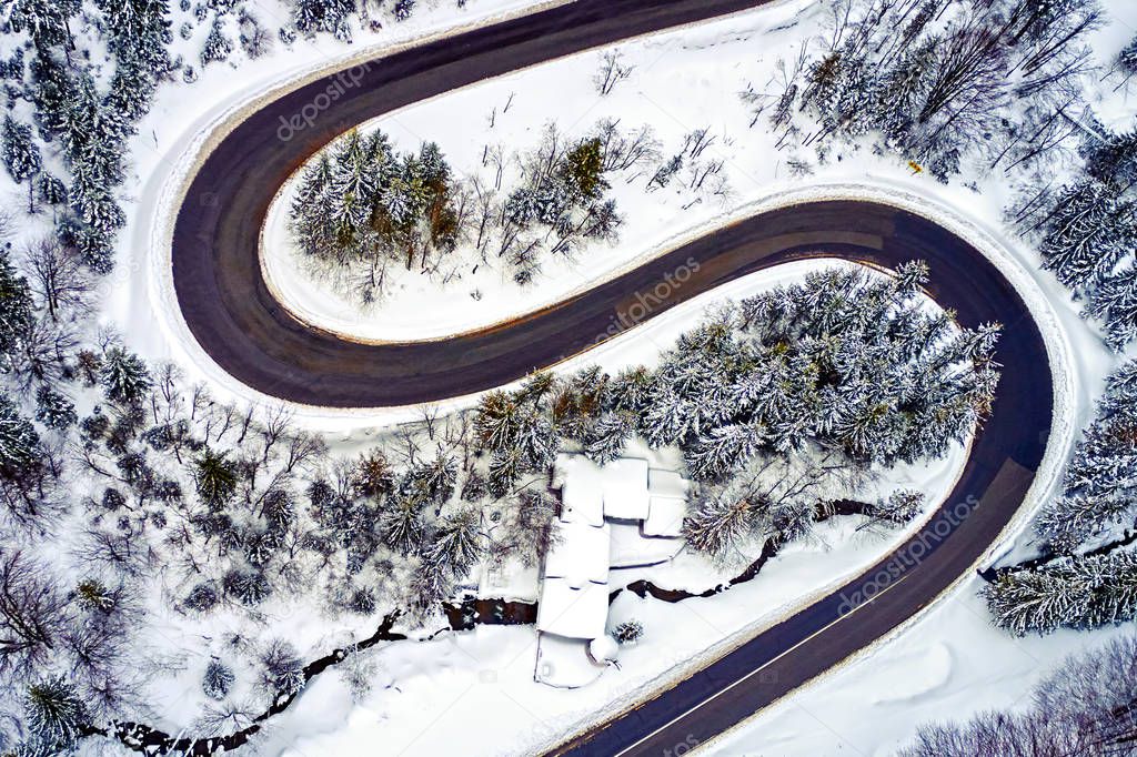 The aerial view of winding road from high mountain pass with snow-covered trees in Transylvania, Romania, Curved road view by drone in the winter time