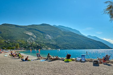 Torbole, İtalya-09 Ekim 2018: insanlar plajda şezlong üzerinde oturan ve yaz saati, görünümü dağlarla çevrili güzel Lake Garda Garda Gölü hayran