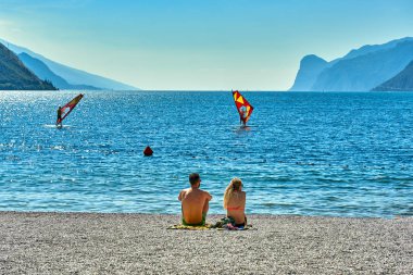 Torbole, İtalya-09 Ekim 2018: insanlar plajda şezlong üzerinde oturan ve yaz saati, görünümü dağlarla çevrili güzel Lake Garda Garda Gölü hayran