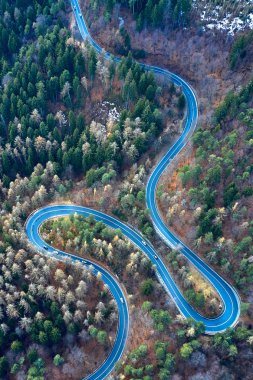 The aerial view of winding road from high mountain pass with trees in Transylvania, Romania, Curved road view by drone in the autumn-winter time clipart