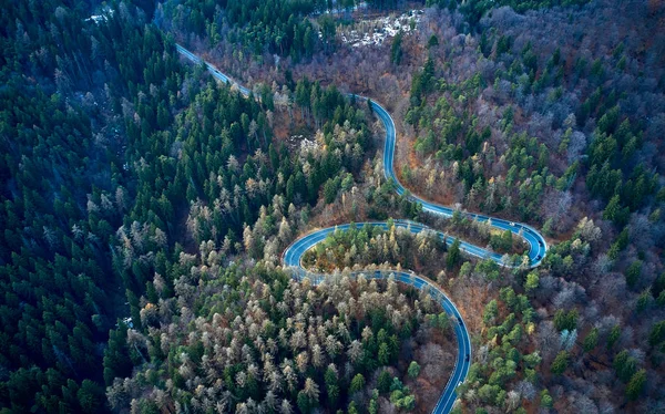 The aerial view of winding road from high mountain pass with trees in Transylvania, Romania, Curved road view by drone in the autumn-winter time