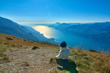 Monte Baldo'dan güzel Garda Gölü'ne hayran olan güzel küçük çocuk, dağlarla çevrili muhteşem Garda gölünün panoraması