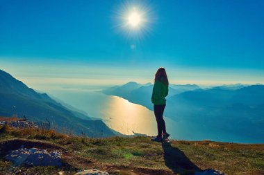Monte Baldo'daki güzel Garda Gölü'ne hayran olan güzel bir kadın, dağlarla çevrili muhteşem Garda gölünün panoraması