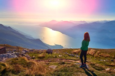 Monte Baldo'daki güzel Garda Gölü'ne hayran olan güzel bir kadın, dağlarla çevrili muhteşem Garda gölünün panoraması
