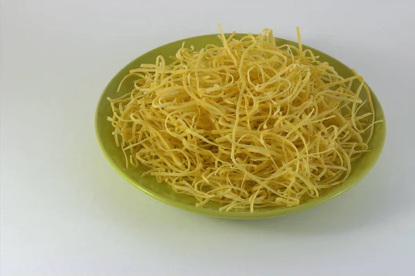 Dry homemade noodles on a green flat plate on a white background. Prepared for boiling water