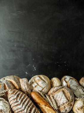 Fırın durak - altın rustik huysuz somun ekmek ve siyah kara tahta arka plan üzerinde maruz buns. Ücretsiz kopya (metin) alanı ile poster düzeni.