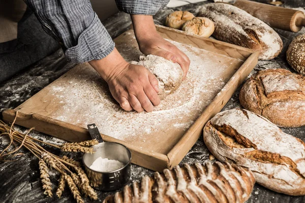 Baker\'s hands kneading raw dough on pastry board. Making whole grain loaf of bread - small bakery scenery.