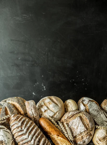 Fırın durak - altın rustik huysuz somun ekmek ve siyah kara tahta arka plan üzerinde maruz buns. Ücretsiz kopya (metin) alanı ile poster düzeni.