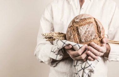 Rustik huysuz somun ekmek ve buğday bir güçlü baker adamın elinde - portre. Küçük işletmeler ve yavaş gıda kavramı. Beyaz arka plan ile ücretsiz (kopya) metin alanı.