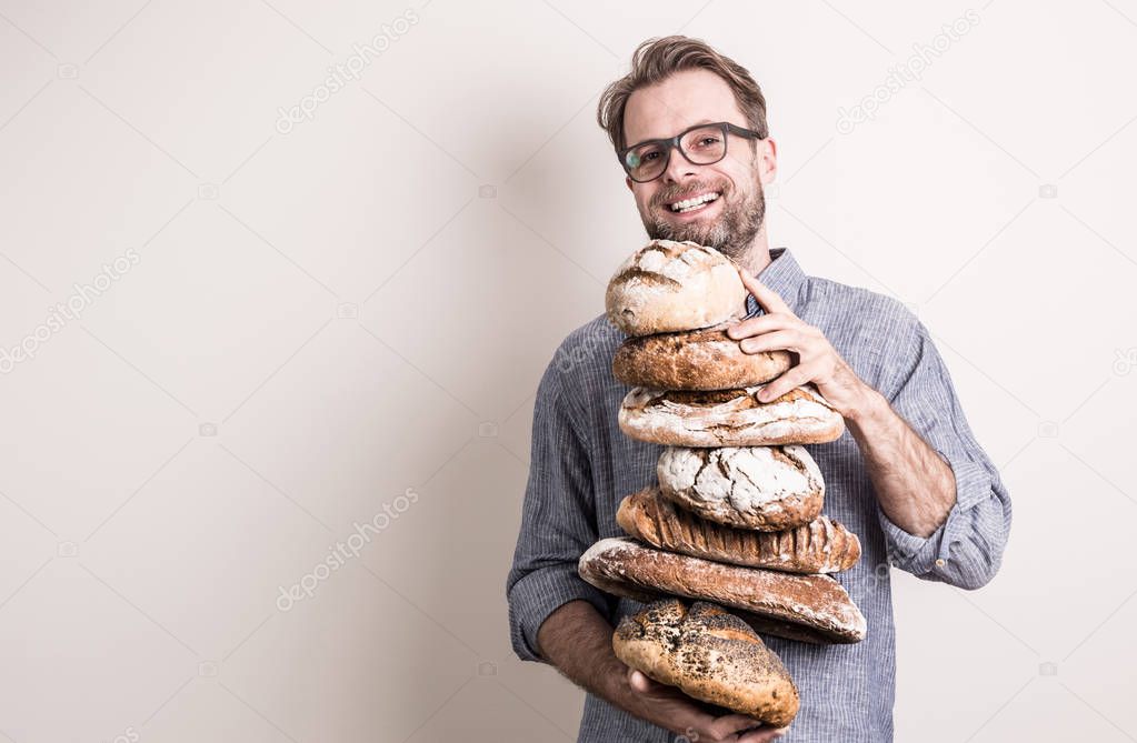 Happy smiling baker man holding pile of rustic crusty loaves of bread. Small business and slow food concept. White background with free (copy) text space.