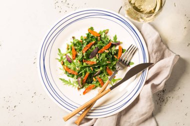 Salata arugula (rucola), karamelize havuç, soğan ve ayçiçeği tohumu ile. Yukarıdan yakalanan plaka (üst görünüm, düz yatıyordu). Gri taş arka plan.