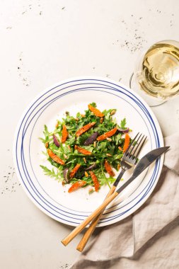 Salata arugula (rucola), karamelize havuç, soğan ve ayçiçeği tohumu ile. Yukarıdan yakalanan plaka (üst görünüm, düz yatıyordu). Gri taş arka plan. Boş metin alanı ile düzen.