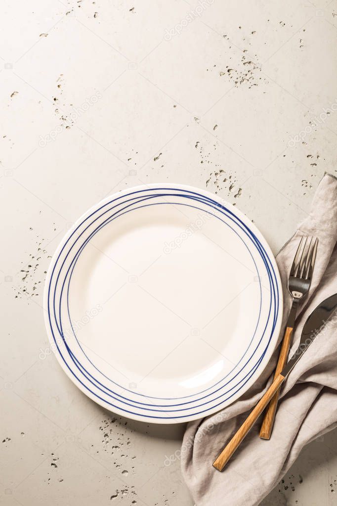 Empty white plate, napkin and cutlery on grey stone background. Composition captured from above (top view, flat lay), layout with free text (copy) space.