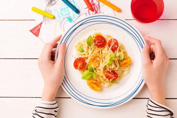 Питание (ужин) в руках ребенка - спагетти с помидорами черри — стоковое фото