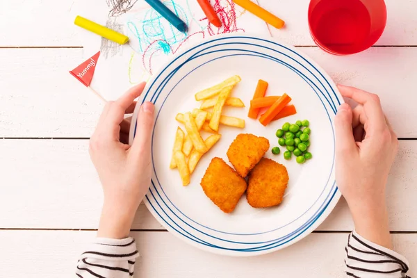 Meal (dinner) in child's hands - chicken nuggets, fries, green p — Stock Photo, Image