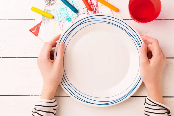 Table setting for kids - empty plate in child's hands — Stock Photo, Image