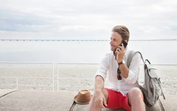 Turysta z plecaka rozmawia na telefon komórkowy nad morzem. — Zdjęcie stockowe