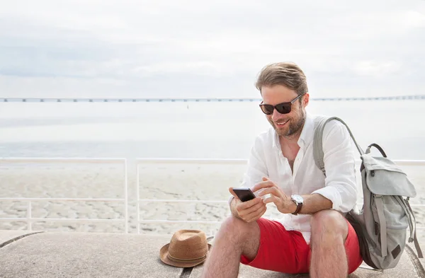 Turystyczny człowiek z plecaka patrząc na telefon komórkowy na zewnątrz przez — Zdjęcie stockowe