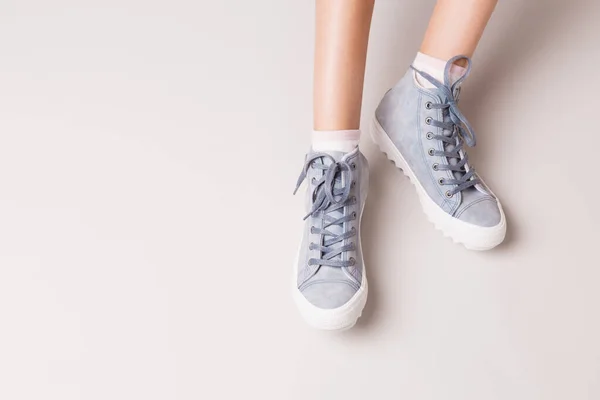 Pastel blauwe sneakers op benen. Casual schoeisel op grijs. — Stockfoto