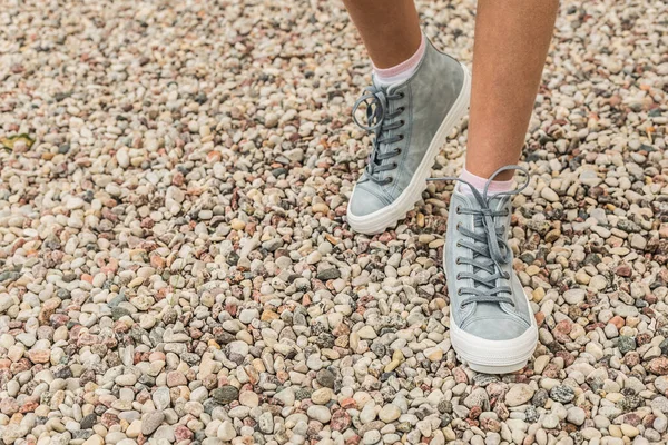 Pastel blauwe sneakers op benen buiten, stenen strand als achtergrond — Stockfoto