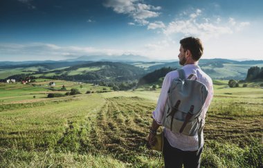 Güzel tepelerin önünde sırt çantalı beyaz bir turist dikiliyor. Eğlence, yürüyüş ve manzaraya hayran olmak - yaz tatili (tatil) aktiviteleri.